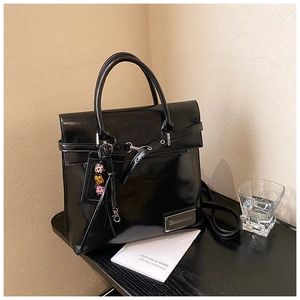 Détail d'un sac à dos noir brillant avec rabat, boucle en métal et breloque en perles