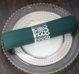Detail of silver hollowed floral napkin ring on a dark green napkin and ceramic plate