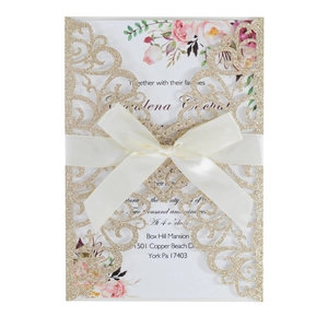Detail of laser-cut floral wedding invitation with gold glitter cover and satin ribbon bow