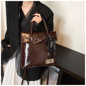 Detail of dark brown glossy patent leather bag with decorative buckle and metal plaque