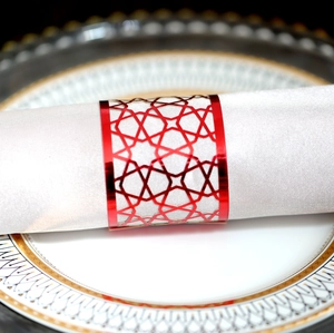 Detail of red metal napkin ring with laser-cut geometric pattern on white fabric