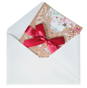 Detail of glitter rose gold laser cut wedding invitation with red silk ribbon and envelope