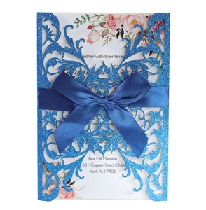 Macro detail of laser-cut blue glitter invitation with floral insert and satin bow ribbon