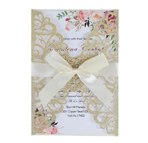 Detail of laser-cut glitter wedding invitation with elegant satin bow and floral insert