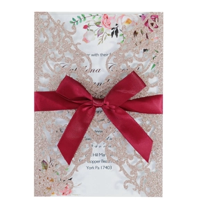 Close-up of laser-cut rose gold glitter wedding invitation with burgundy satin ribbon