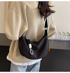 Detail of black half-moon crossbody bag with orange logo tag and contrast knotted zipper pull