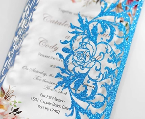 Macro shot of glittery dark blue laser-cut floral wedding invitation with white insert