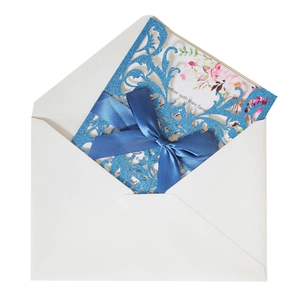 Macro view of blue glitter laser-cut floral wedding invitation with satin bow and envelope