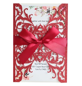 Intricate red laser-cut glitter wedding invitation with elegant satin bow and floral insert