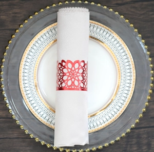 Detail of red laser-cut floral napkin ring on a white napkin with luxury dinnerware
