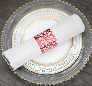 Close-up of a glossy red napkin ring with a hollow floral pattern on a fabric napkin