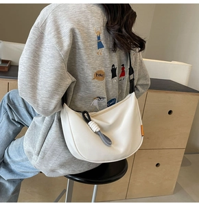 Detailed view of white crescent bag featuring black adjustable strap and woven rope charm