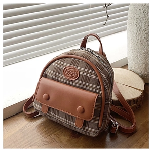 Detail of vintage brown plaid mini backpack with leather trim on a wooden tabletop