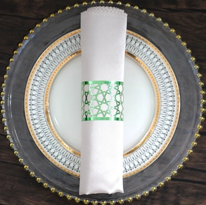 Macro view of green metal napkin ring with geometric laser-cut patterns on a white silk napkin