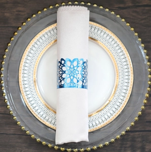 Detail of laser-cut floral metal napkin ring in electroplated blue with silk napkin