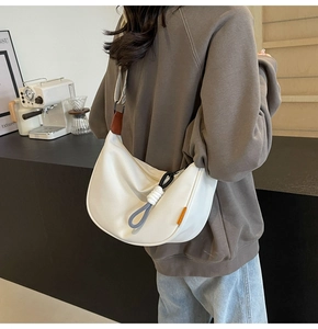 Detail of white crescent canvas bag with decorative woven knot zipper on model