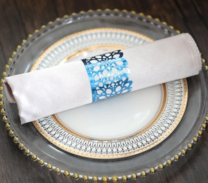 Macro view of blue laser-cut napkin ring on silk napkin with elegant gold-rimmed tableware