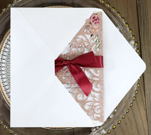 Detail of laser-cut glitter rose gold invitation set with burgundy ribbon and floral card