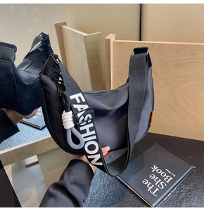 Detail of black crescent canvas bag with FASHION lettered strap and woven charm