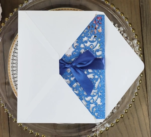 Detailed laser-cut glitter wedding invitation with blue ribbon and elegant white envelope