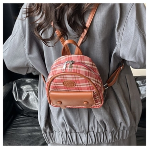 Detailed view of mini plaid backpack with red-brown fabric and leather straps on model
