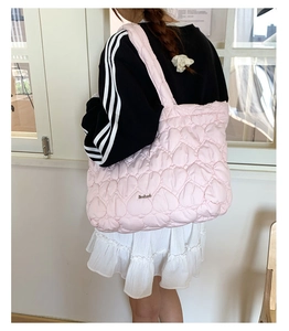 Detail of pink heart quilted tote bag with silver logo tag and wide shoulder strap