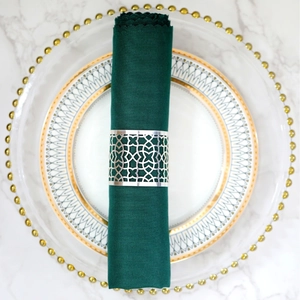 Flat lay of a silver geometric cut-out napkin ring with deep green linen napkin on a plate