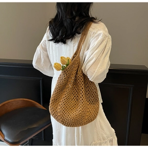 Detail of a brown crochet mesh tote bag worn by a model in a white lace dress