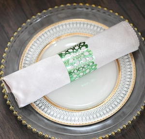Detailed view of a green laser-cut floral napkin ring on a satin pink napkin with gold rim plate
