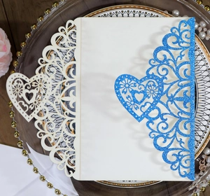 Detail of laser-cut wedding invitation with blue glitter and elegant white heart pattern