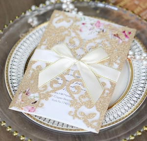 Vista macro dell'invito di nozze dorato con glitter, intaglio laser e fiocco di raso bianco