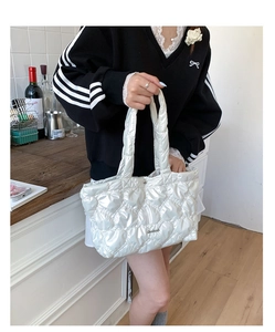Detail shot of pearl white quilted tote bag featuring metallic logo and padded handles