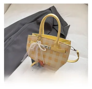 Detail of yellow checkered mini handbag with gold metal lock and pearl bow charm