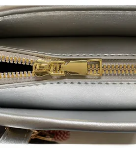 Detail of smooth gold metal zipper and textured silver-grey leather on shoulder bag