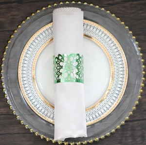 Detail of laser-cut green floral napkin ring on a white napkin over elegant dinnerware