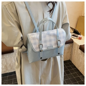 Close-up of a light blue leather backpack with blue plaid flap and silver buckles