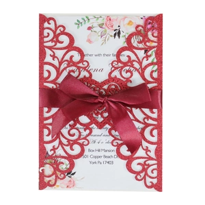 Detail of red glitter laser-cut wedding invitation with burgundy ribbon and floral card