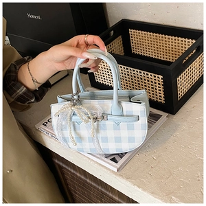 Detail of blue plaid bucket bag with pearl strap and lace bow on a marble table