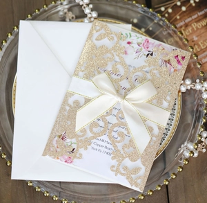 Dettaglio invito di nozze glitter oro intagliato al laser con inserto floreale e fiocco crema