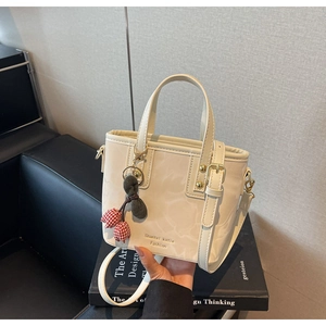 Detail of cream white leather bucket bag with red cherry charm and golden hardware