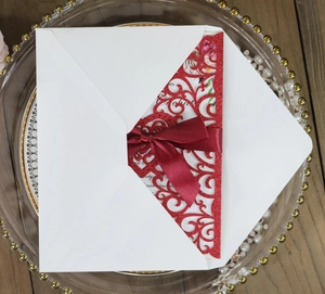 Macro detail of laser-cut wedding invitation with burgundy glitter card and satin bow