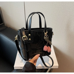Close-up of black crocodile-embossed bucket bag with gold rivets and cherry charm