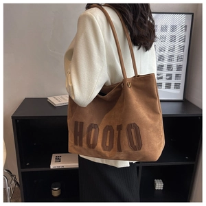 Detail of dark brown faux suede tote bag with HOOTO embroidery worn on shoulder