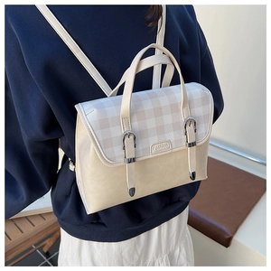 Detail view of cream white backpack with grey plaid flap and adjustable straps in use