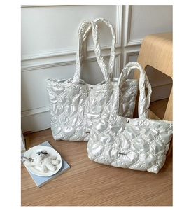 Macro shot of white heart-quilted glossy nylon tote bag with handmade metal logo detail