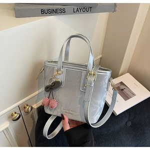 Detail of silver gray PU leather handbag with cherry charm and brand logo on a side table