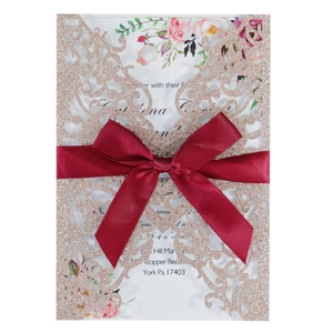 Laser cut rose gold glitter wedding invitation with a deep red satin bow and floral insert