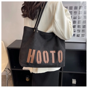 Detail view of a large black tote bag with brown HOOTO leather patch on a model