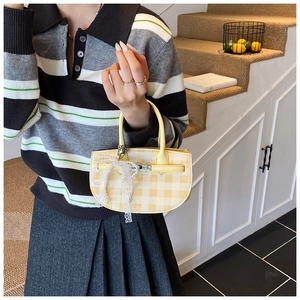 Detailed shot of yellow plaid bucket bag featuring a pearl lace bow charm and metal clasp