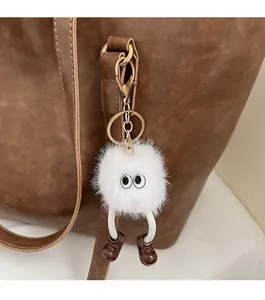 Close-up of a white fluffy monster charm with large eyes on a brown leather tote bag
